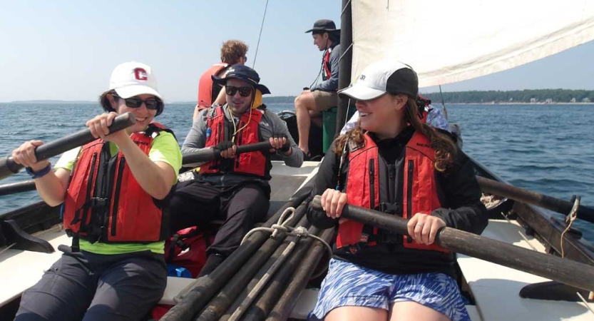 A group of students wearing life jackets hold the oars of a sailboat 